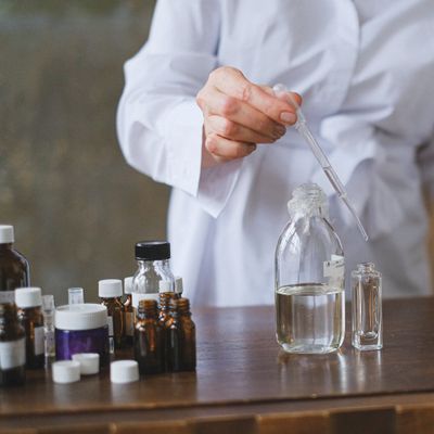 Person in lab coat using dropper to transfer liquid into clear glass bottles on a table.